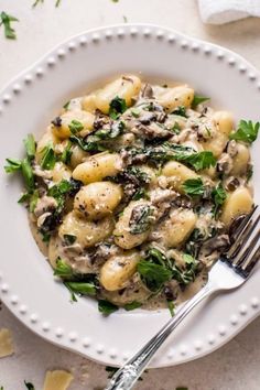 a white plate topped with pasta covered in mushroom and spinach sauce next to a fork