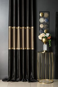 a black and gold curtain in front of a vase with flowers on it next to a mirror