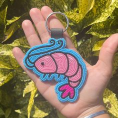 a hand holding a beaded keychain with a pink fish design on it