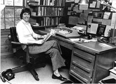 a woman sitting at a desk in front of a bookshelf filled with books