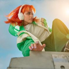 a woman with red hair and headphones sitting on top of a metal box in the sun