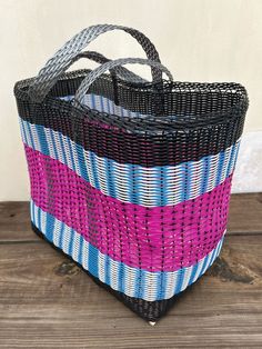 a black, blue and pink basket sitting on top of a wooden table next to a white wall