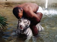 a man in the water with a white tiger on his chest and one arm wrapped around him