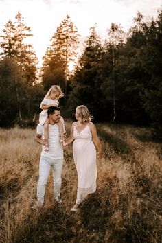 a man holding a baby while standing next to a woman in a field with trees