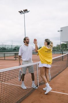 a man and woman standing on a tennis court holding their hands up to each other