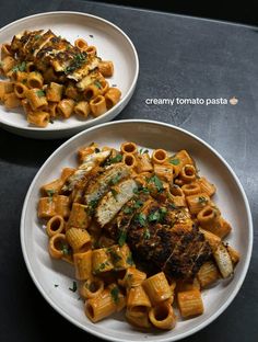 two white plates filled with pasta and meat on top of a black countertop next to each other