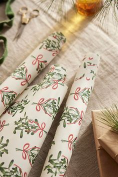 napkins with bows and holly on them are sitting on a table next to pine branches