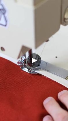 someone is using a sewing machine to sew something on the red fabric with their hands