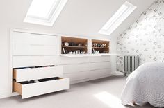 a white bed sitting under a skylight in a bedroom next to a dresser with drawers