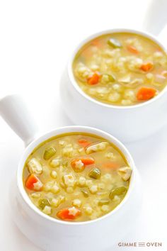 two bowls of soup with carrots, celery and peas on a white surface