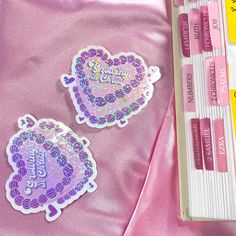 two heart shaped stickers sitting on top of a pink sheet