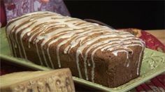 a loaf of chocolate cake with icing on a green plate next to a wooden block