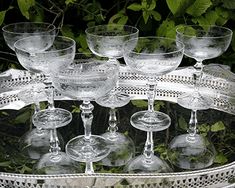 several wine glasses sitting on top of a glass platter in the middle of a garden