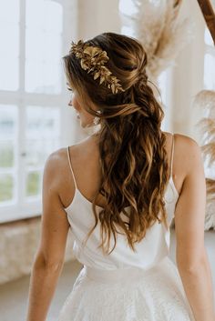 a woman with long hair wearing a white dress and gold leaves in her hair is looking out the window