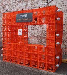 several orange crates stacked on top of each other in front of a brick wall with a sign that reads ticket collection