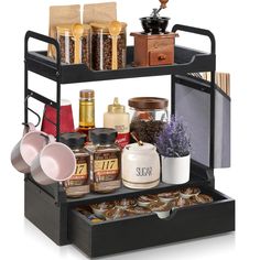 an assortment of coffee and tea items on a black shelf with drawers, cups, saucers and spoons