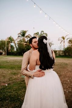 a bride and groom embracing each other in front of string lights at their backyard wedding