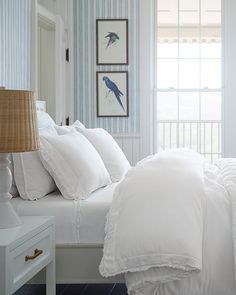 a bed with white linens and pillows in a blue room next to a window