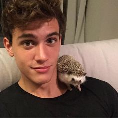 a young man is holding a hedgehog on his shoulder