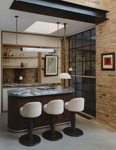 three white stools sit in front of an island with marble counter top and brick wall