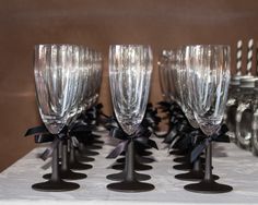 four wine glasses with black bows are sitting on a table next to silver candlesticks