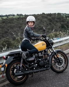 a woman sitting on top of a yellow motorcycle next to a road with trees in the background