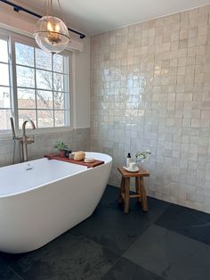 a large white bath tub sitting next to a window in a bathroom with black tile flooring