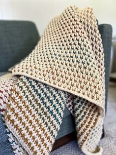 a crocheted blanket folded over a couch with a blue chair in the background