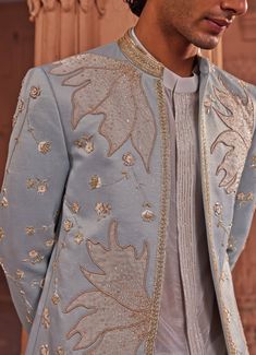 Presenting the Aqua Blue Applique Sherwani Set, a masterpiece that exudes timeless charm and sophistication. Crafted from luxurious jacquard silk, this aqua blue sherwani showcases a stunning tissue applique technique, beautifully complemented by intricate zardozi and dabka embroidery. The design features large, graceful leaf-like motifs and delicate floral details, meticulously placed to create a visually striking ensemble. Paired with a front open white kurta, adorned with fine detailing on the placket, adding an extra touch of elegance. Completed with complementary white pants, this outfit is perfect for those who appreciate a seamless blend of traditional craftsmanship and modern style. Ideal for Mehndi, Sangeet, or as wedding guest attire, this sherwani set ensures you make a lasting Sherwani Embroidery Design, Indian Motifs Traditional, Groom Sherwani Indian, Blue Sherwani, Sherwani Groom, White Kurta, Indian Wedding Wear, Men Stylish Dress, Guest Attire