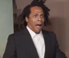 a man with dreadlocks in a suit and tie is making a funny face