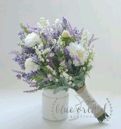 a bouquet of white and purple flowers in a mason jar with lace on the handle