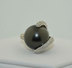 This is an impressively large pearl ring. The pearl is a south Sea Black Tahitian Pearl. The pearl is drilled and mounted with pave diamond accents. The small prong is drilled on the side and the fingers of diamonds are securing the pearl with no movement. This pearl is big, measuring in at 15.5 mm. It is a deep grey/black, perfectly round. There are a couple of natural dimples on the side not the top of the pearl as photographed The setting is 14K White gold, not hallmarked but tested and guara Formal Black Tahitian Pearl Ring, Tahitian Pearl Ring With Diamond Accents Fine Jewelry, Classic Tahitian Pearl Ring With Diamond Accents, Fine Jewelry Tahitian Pearl Ring With Diamond Accents, Tahitian Pearl Ring With Diamond Accents, Luxury Tahitian Pearl Ring With Diamond Accents, Elegant Tahitian Pearl Ring With Diamond Accents, Formal Tahitian Pearl Ring With Diamond Accents, Tahitian Pearl Ring