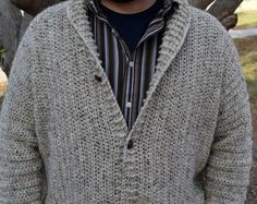 a man standing in front of a tree wearing a knitted sweater and hat with his hands in his pockets