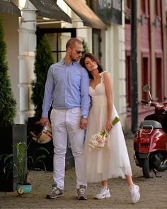 a man and woman standing next to each other in front of a motorcycle parked on the street