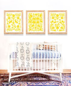 a baby crib in front of three framed art prints on the wall above it