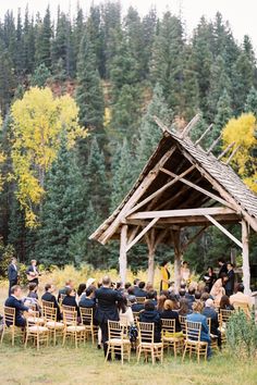 a group of people sitting around a wooden structure in the middle of a forest filled with trees