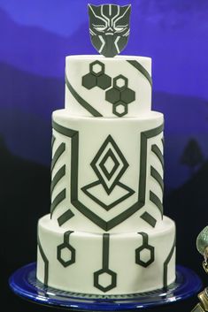 a three tiered cake with black and white designs on the top, sitting on a blue plate