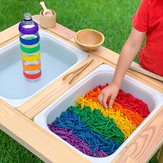 a child's hand is in the middle of a tray with rainbow colored beads