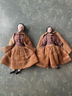 two dolls are laying on the floor next to each other, one is wearing a brown dress