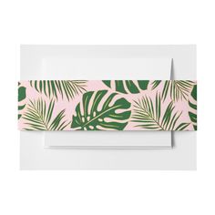 a white envelope with green palm leaves on the front and bottom, along with a matching ribbon