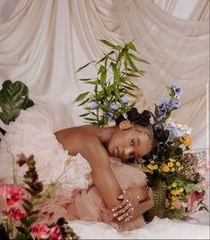 a woman in a pink dress sitting on a bed with flowers and greenery around her