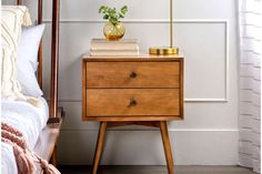 a nightstand with two books and a vase on it next to a bed in a bedroom