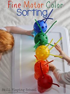 two children playing with colorful plastic balls on a white tray that says fine motor color sorting