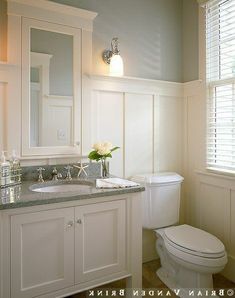 a white toilet sitting next to a sink in a bathroom under a window with shutters