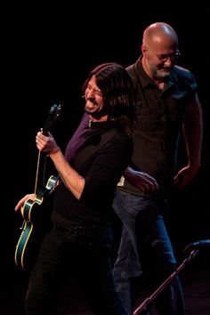 two people on stage one holding a guitar and the other singing