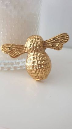 a gold bird figurine sitting on top of a white table next to a cup