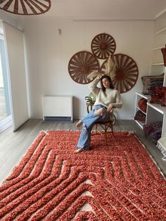 a woman sitting in a chair on top of a red rug next to a window