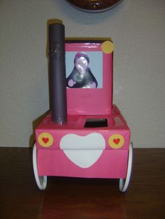 a pink toy car with a stuffed animal in it's seat on top of a wooden table