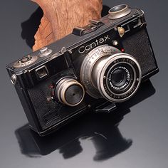 an old camera sitting on top of a table next to a tree branch with the word contax written on it