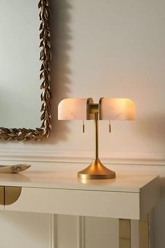 a table lamp sitting on top of a white desk next to a mirror and wall